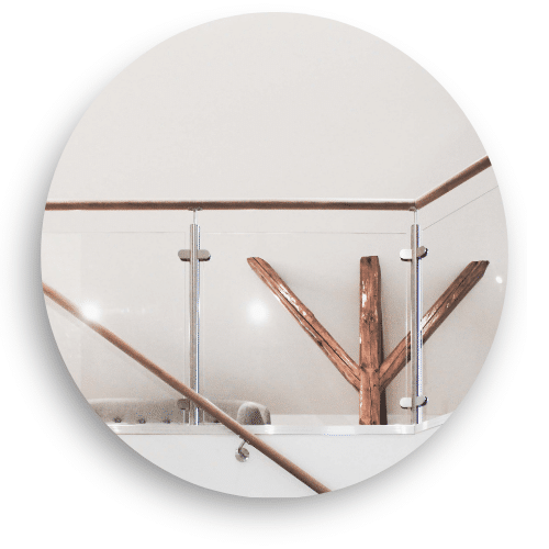 Et innendørs rekkverk i glass med rustfrie stolper og håndløper i tre. Rekkverket omkranser en åpen flate, der en dekorativ tredetalj gir et varmt og naturlig preg i interiøret.