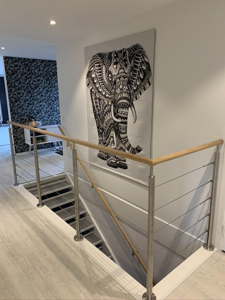 Innendørs vajerrekkverk i rustfritt stål med trehåndløper rundt trappeoppgang i lyst, moderne interiør