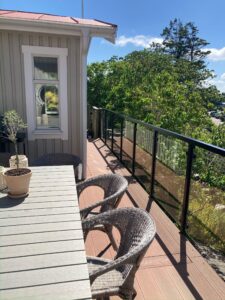 Svart glassrekkverk ved terrassefasade med spisegruppe og stoler – perfekt gelender til altan med hageutsikt.