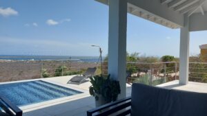 Basseng med rekkverk i rustfritt stål og horisontale vaiere, plassert på terrasse med panoramautsikt over kyst og hav.