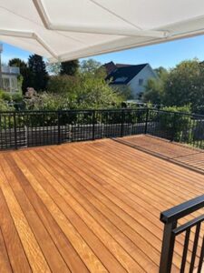 Svart altanrekkverk i smijern rundt terrasse med markise, grønn beplantning og solrikt uteområde.