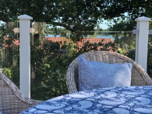 Nærbilde av terrasse med hvitt gelender i aluminium, klart glass, rottingmøbler og utsikt mot innsjø.