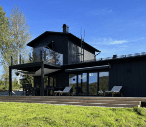 Moderne glassrekkverk med svarte stolper og sotet glass på øvre terrasse ved mørk trefasade.