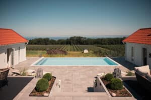 Moderne stolpefritt glassrekkverk rundt infinitybasseng med utsikt mot hav, eplehage og åpent kulturlandskap.