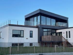 Stolpefritt glassrekkverk rundt takterrasse på moderne villa med store vinduer og minimalistisk design.