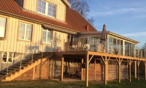 Glassrekkverk i rustfritt stål og klart glass montert langs utendørs trapp og terrasse i tre – med vinterhage.